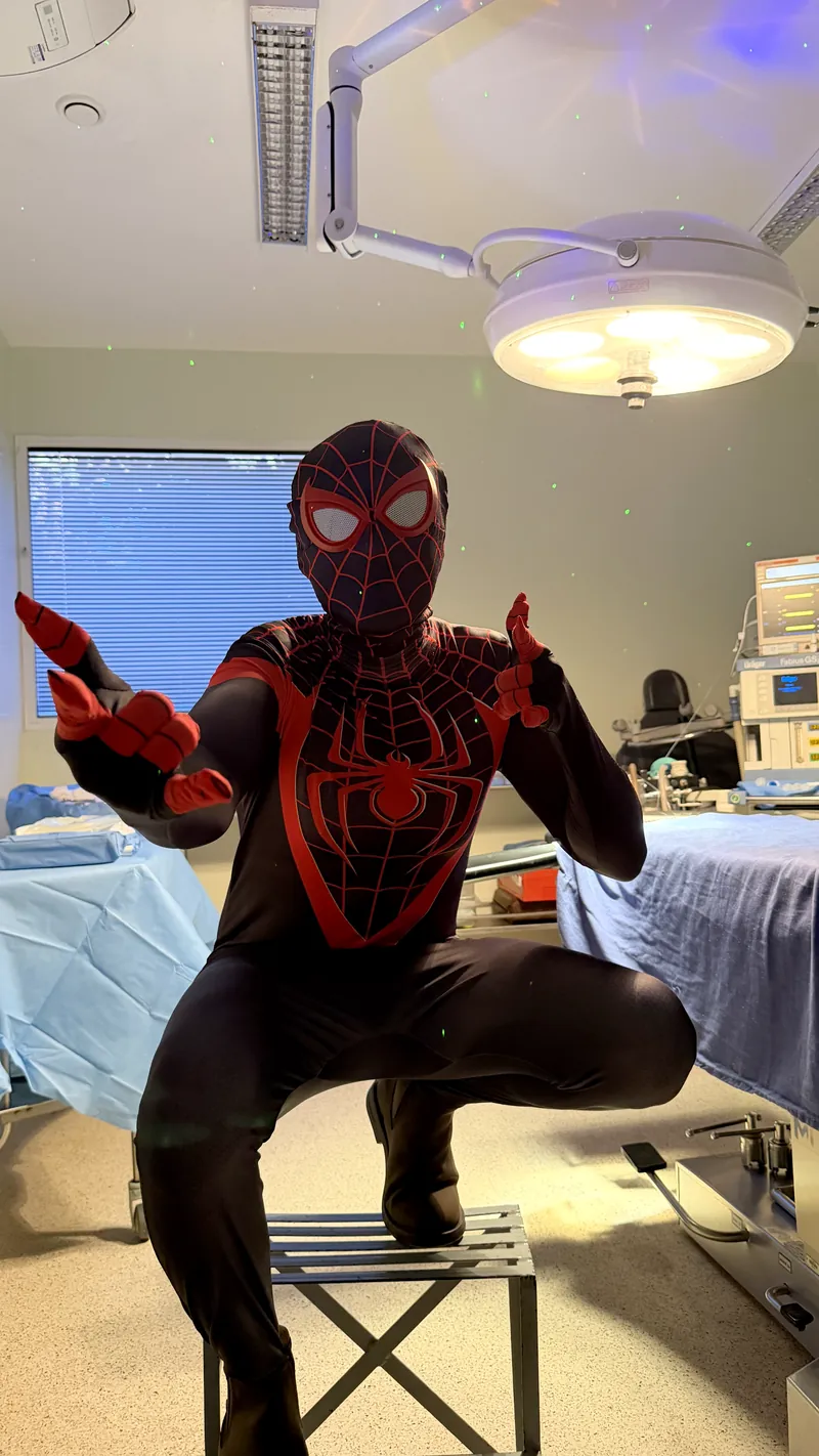 Super-herói com traje do Homem-Aranha agachado no centro cirúrgico, sob o foco de luz